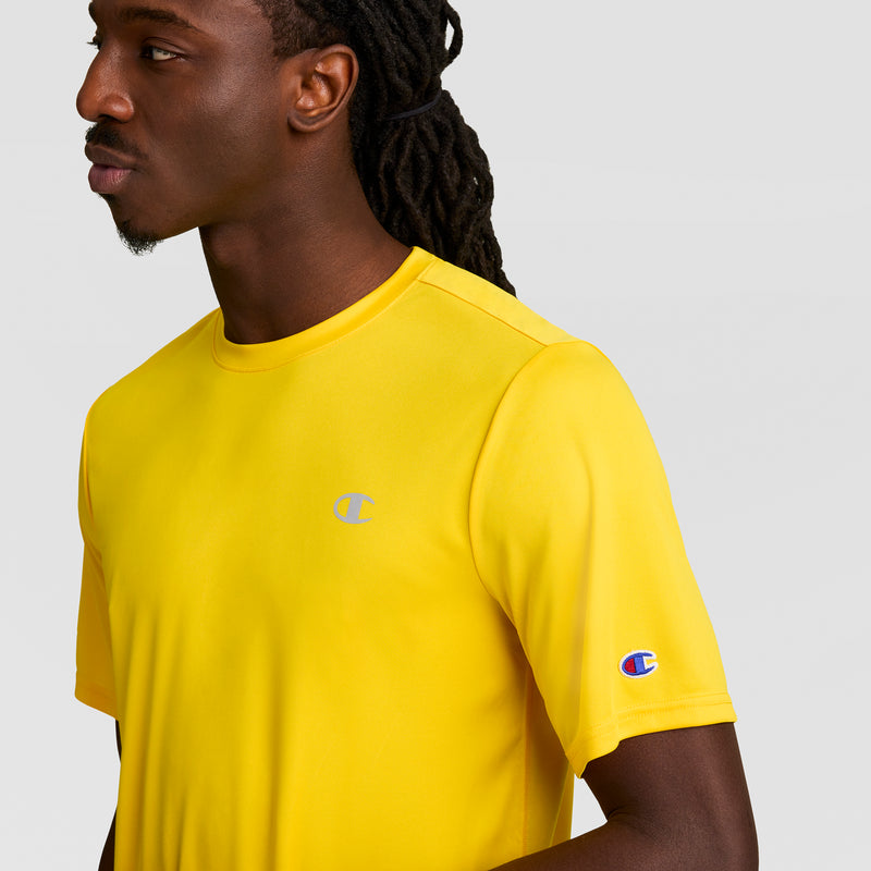 A man wears the Champion Sport T-Shirt, Reflective C Logo in bright yellow, featuring chest and sleeve logos. The athletic men's tee stands out against a plain light gray background.