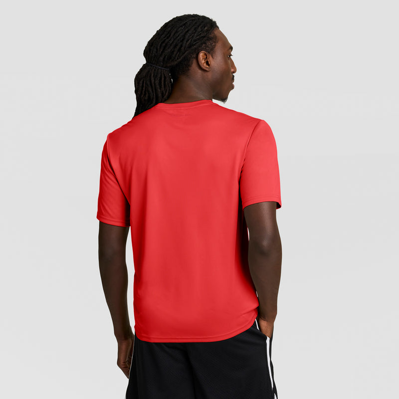 A person with long, braided hair stands facing away in a Champion Sport T-Shirt with a reflective C logo and black athletic shorts with white stripes, set against a light gray background.