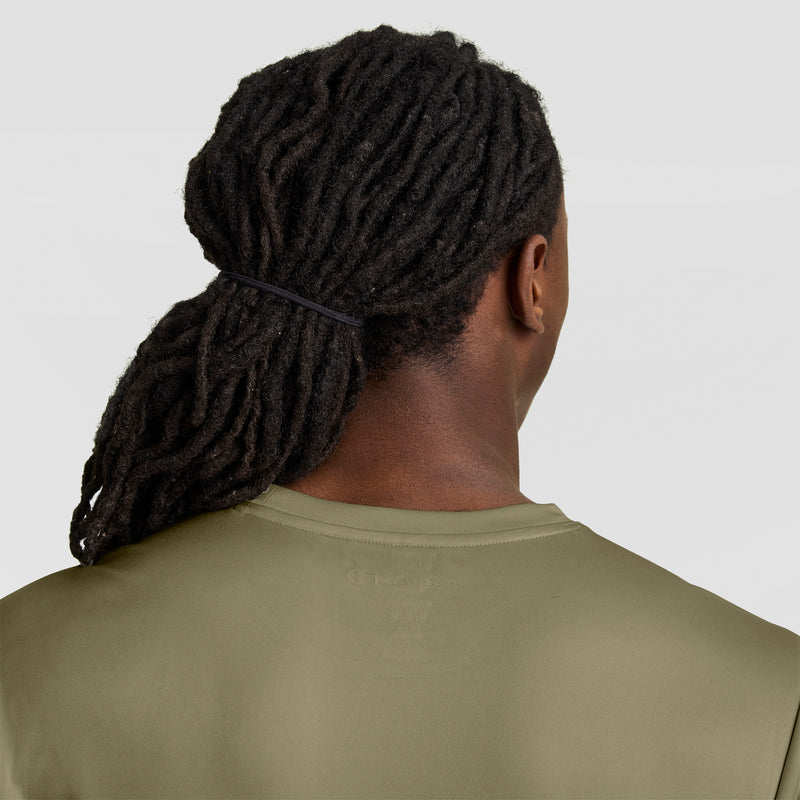 A person with long, dark dreadlocks tied back, shown from behind, wears a Champion Sport T-Shirt with Double Dry technology and a reflective C logo in olive green against a plain light background.