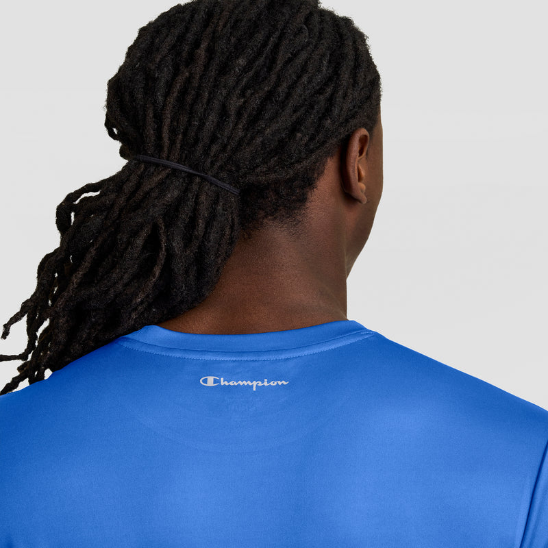 A person with long, dark, braided hair tied back is seen from behind wearing a bright blue Champion Sport T-Shirt featuring Double Dry technology and a reflective C logo near the neckline for an athletic look.