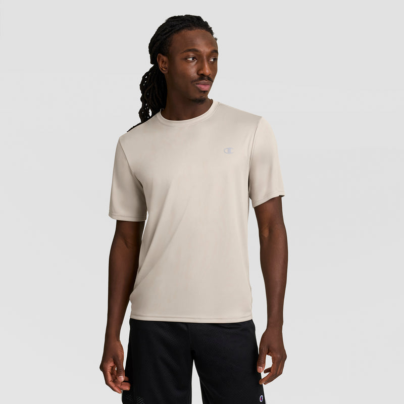 A man with long dark dreadlocks wears a Champion Sport T-Shirt with a reflective C logo, featuring Double Dry technology and anti-odor protection, plus black shorts, standing against a light gray background and looking slightly left.