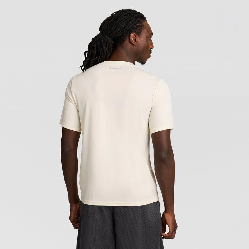 A man with long, dark, braided hair is shown from the back wearing a Champion Sport T-Shirt, Reflective C Logo in off-white and dark shorts. The athletic shirt stands out against a plain, light gray background.