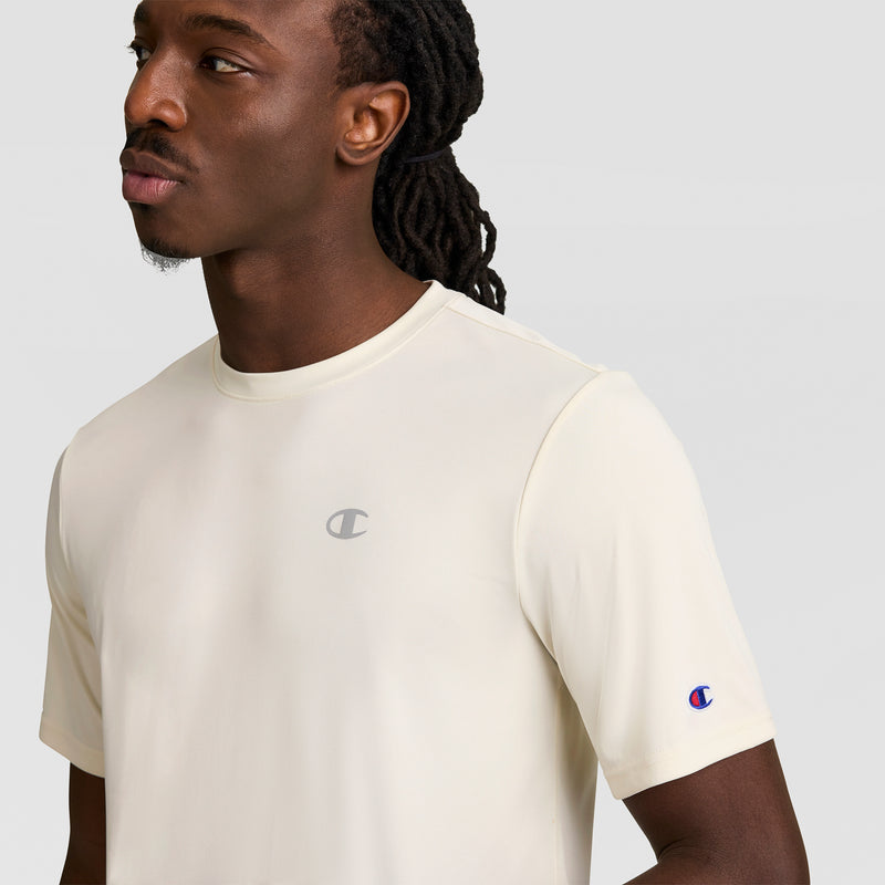 A man with long, dark, braided hair wears a Champion Sport T-Shirt with Reflective C Logo, looking to the side against a plain light gray background.