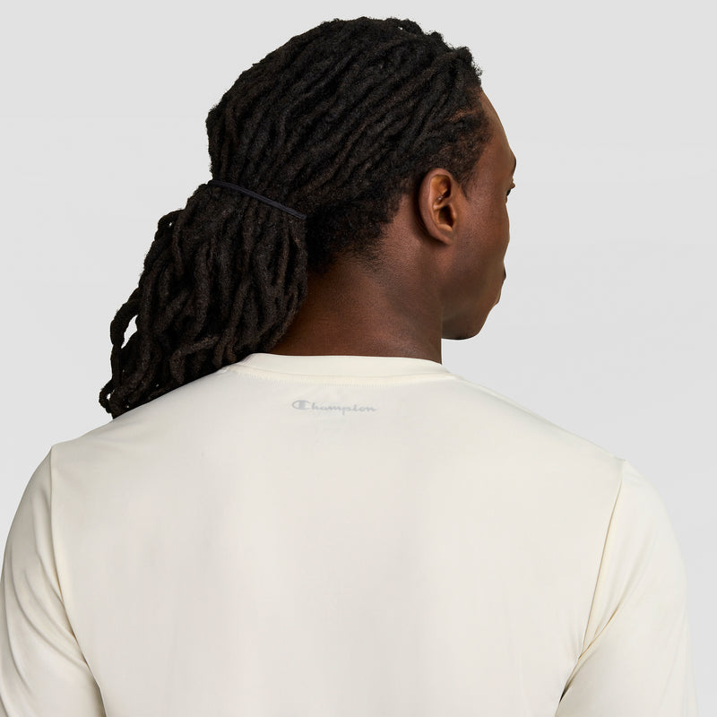 A person with long, dark dreadlocks tied back is seen from behind wearing a Champion Sport T-Shirt, Reflective C Logo, in off-white against a plain light gray background.