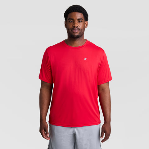 A man stands facing forward, wearing a bright red Champion Sport T-Shirt with Reflective C Logo - Big & Tall and light gray shorts, against a plain light gray background.