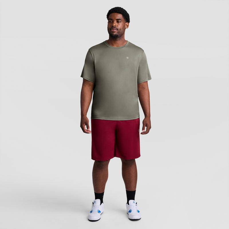 A man faces forward in a Champion Sport T-Shirt with Reflective C Logo - Big & Tall, maroon athletic shorts, black socks, and white sneakers against a plain light gray background.