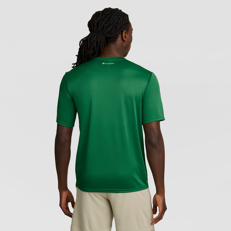 A man with long braided hair is seen from behind, wearing a Champion Sport T-Shirt with Reflective C Logo featuring Double Dry technology and beige shorts, posed against a plain light gray background.