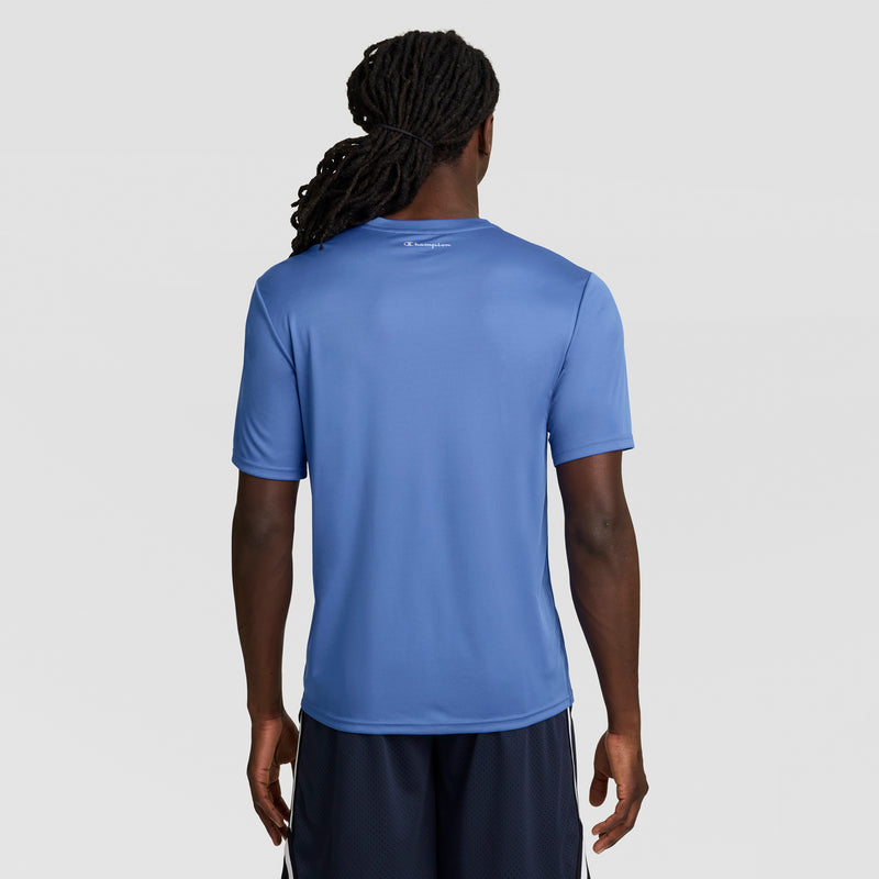 A person with long, tied-back hair is shown from behind, wearing a Champion Sport T-Shirt with a Reflective C Logo and dark shorts, standing against a plain light gray background.