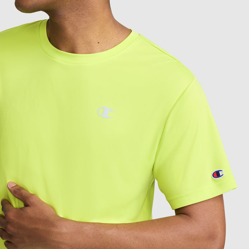 A person wearing a bright yellow-green Champion Sport T-Shirt, Reflective C Logo, featuring the Champion logo on the chest and sleeve, is seen from neck to waist with their left hand resting on their torso.