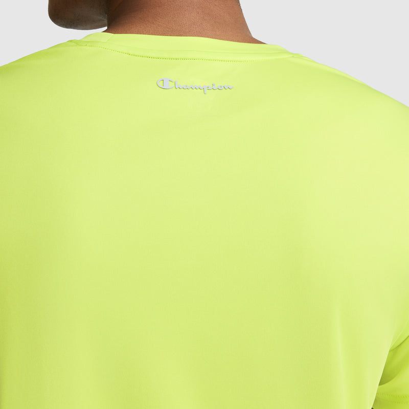 Close-up of the back of a person wearing a bright yellow-green Champion Sport T-Shirt, Reflective C Logo. The small, embroidered reflective Champion logo appears near the top of this men’s athletic shirt.