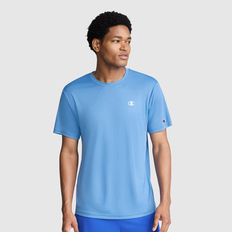 A man wearing a light blue Champion Sport T-Shirt with a Reflective C Logo and blue shorts stands against a plain light gray background, looking to his left.