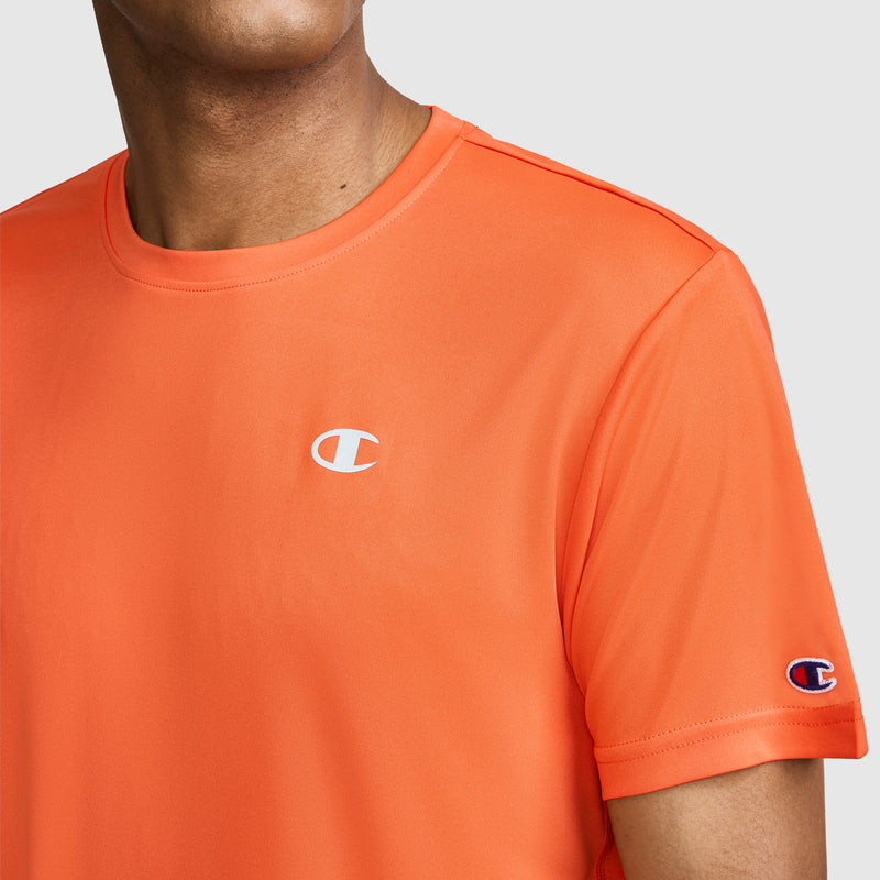 A person wearing a Champion Sport T-Shirt with short sleeves in orange, featuring reflective C logos on the chest and sleeve, shown from the shoulders to mid-torso against a plain background.