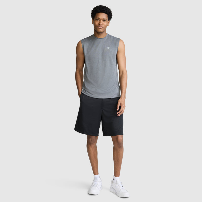 A man stands against a plain background wearing the Champion Sport Muscle Tank with a Reflective C Logo, paired with black shorts and white sneakers. This moisture-wicking sleeveless workout shirt keeps him comfortable as he looks at the camera with his hands by his sides.