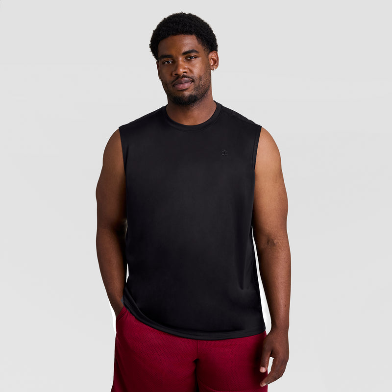 A man stands against a plain gray background, wearing the Champion Sport Muscle Tank with Reflective C Logo - Big & Tall and red shorts. He has short curly hair, a trimmed beard, one arm relaxed at his side, and a neutral expression.