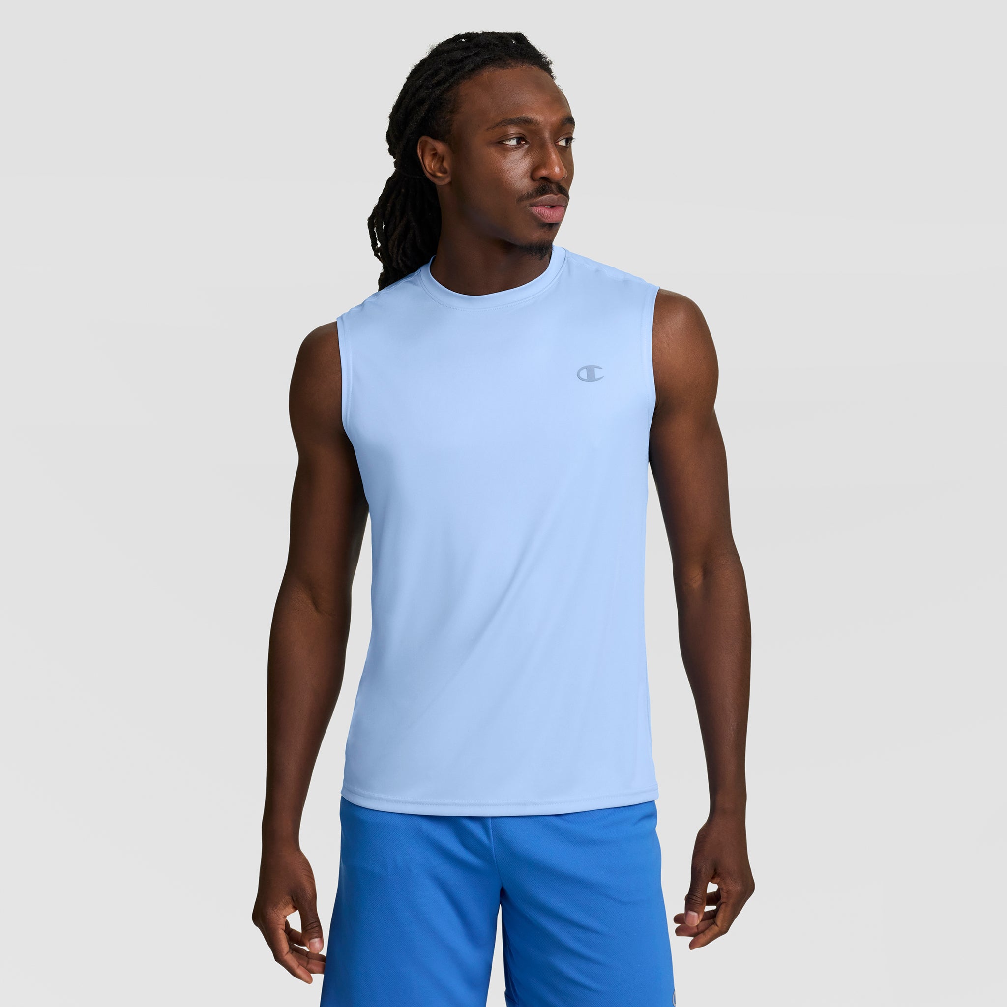A man stands against a light gray background, modeling the Champion Sport Muscle Tank with Reflective C Logo—a comfortable, moisture-wicking workout shirt for men in light blue.