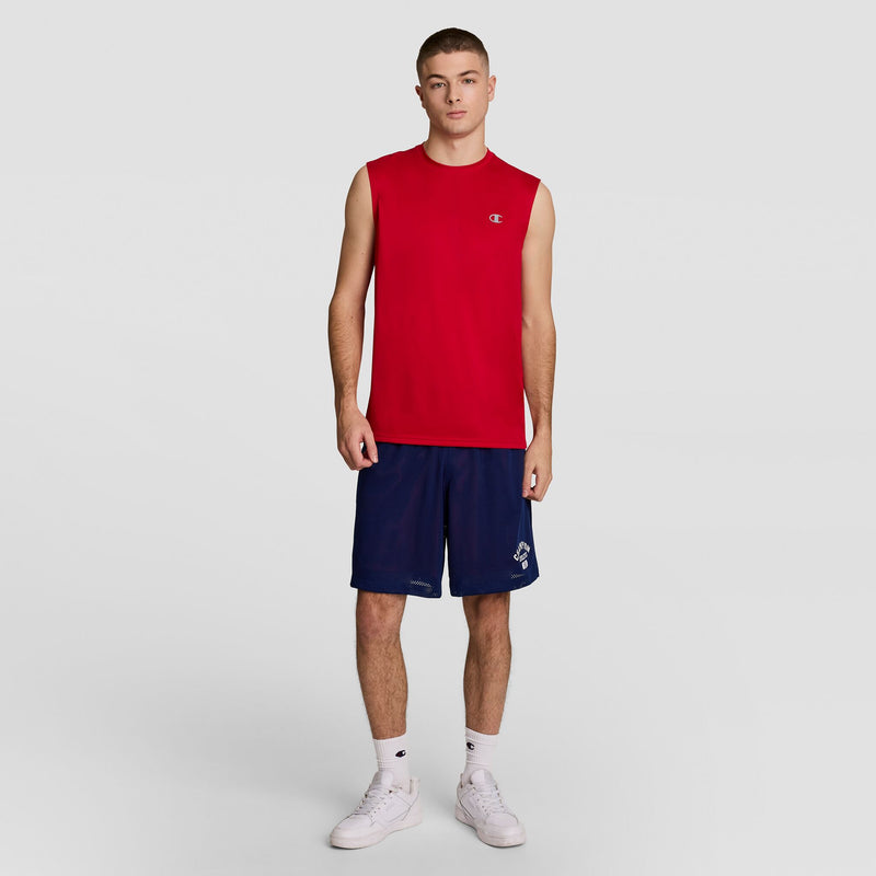 A young man with short hair and a neutral expression stands against a plain background, wearing the Champion Sport Muscle Tank with Reflective C Logo, paired with navy blue shorts, white socks, and white sneakers. One arm is relaxed and the other slightly bent.