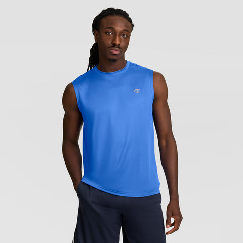 A man with long braids wears a Champion Sport Muscle Tank with a Reflective C Logo and dark shorts, standing with one hand in his pocket against a plain light gray background.