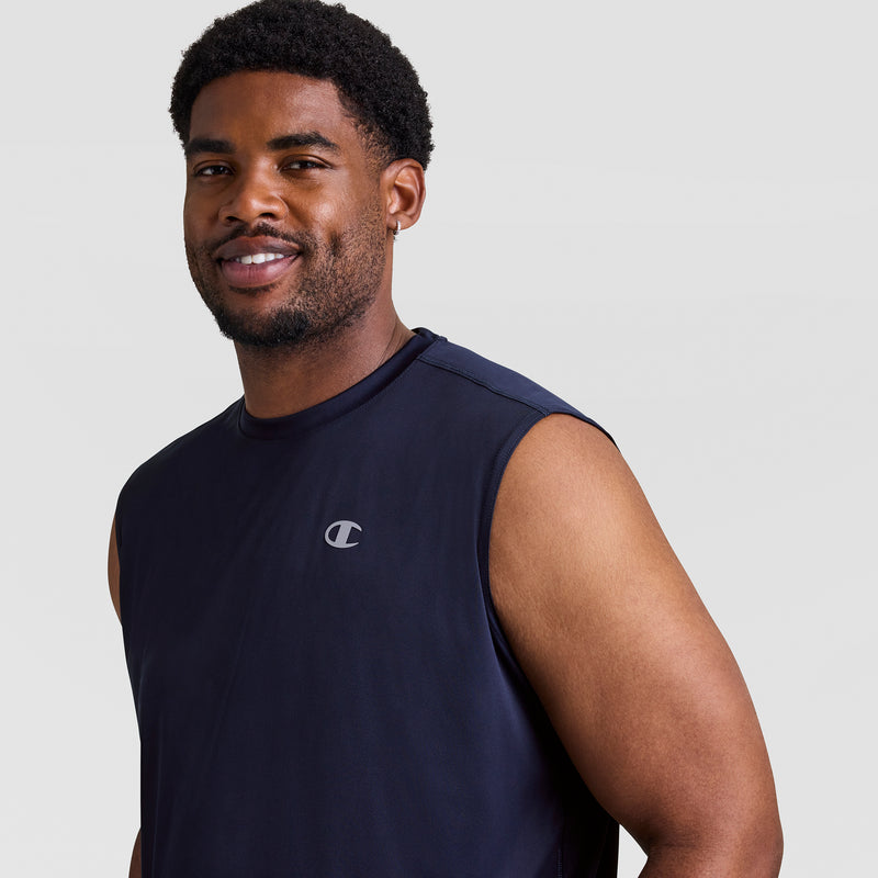 A man with short curly hair and a beard smiles, wearing the Champion Sport Muscle Tank, Reflective C Logo - Big & Tall—a sleeveless navy shirt with a small reflective Champion logo—standing against a plain light gray background.
