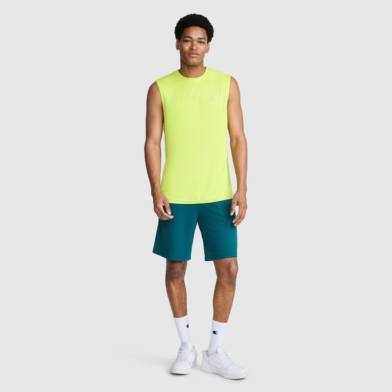 A man stands smiling against a plain light gray background, wearing the Champion Sport Muscle Tank with Reflective C Logo in sleeveless neon yellow for moisture-wicking performance, paired with teal shorts, white socks, and white sneakers.