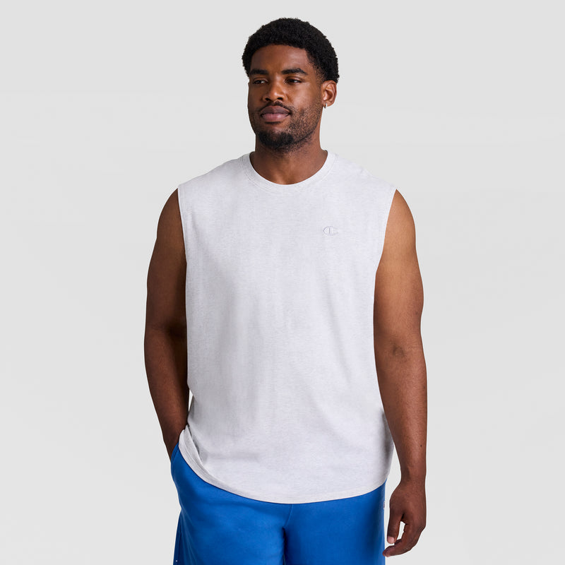 A man wears the Champion Muscle Tank, C Logo - Big & Tall, paired with blue shorts and stands against a plain light gray background, looking slightly to the side with a relaxed expression.