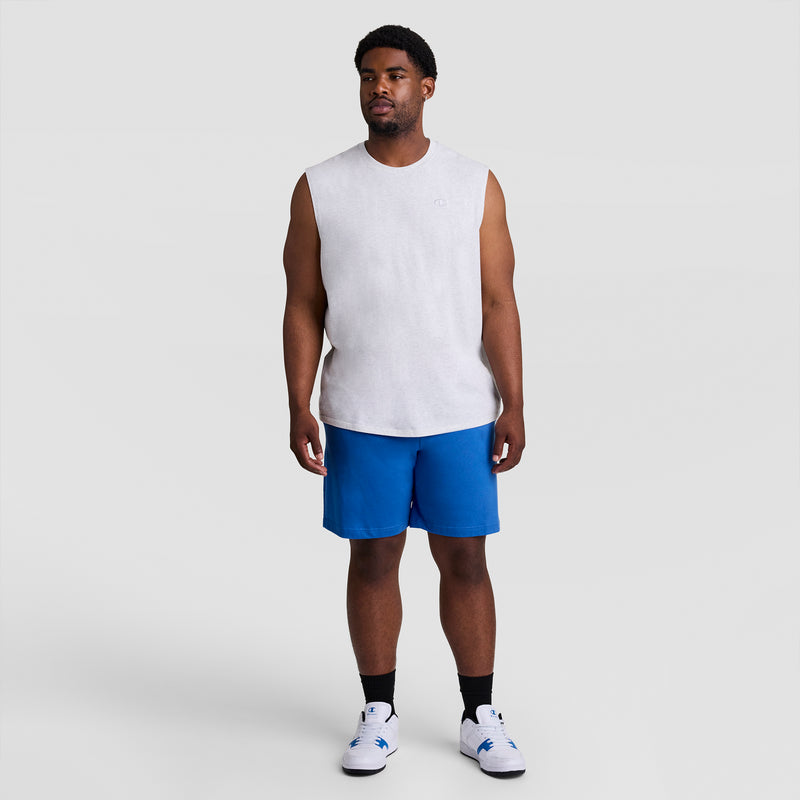 A man stands facing forward in a Champion Muscle Tank, C Logo - Big & Tall, sleeveless and light gray, paired with bright blue shorts, black socks, and white athletic shoes against a plain light gray background.