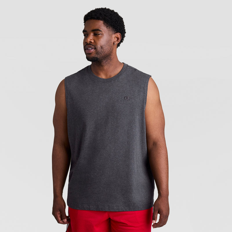 A man wears the Champion Muscle Tank, C Logo - Big & Tall in dark gray with red shorts, standing against a plain light gray background and looking slightly to his left with a relaxed expression.