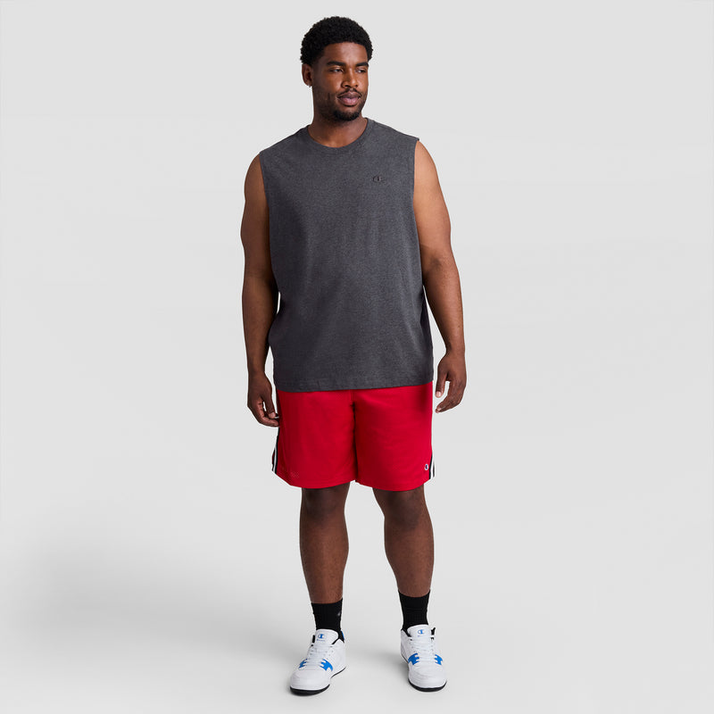 A man wears the Champion Muscle Tank, C Logo - Big & Tall in dark gray, paired with bright red shorts, black socks, and white athletic shoes against a plain light gray background.