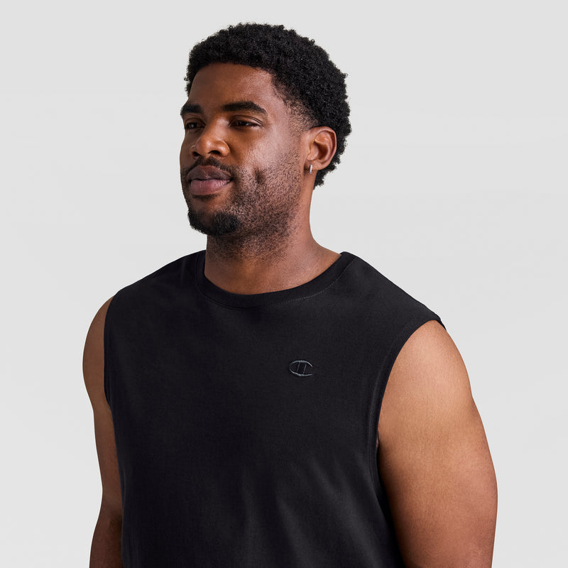 A man with short curly hair and a beard wears the Champion Muscle Tank, C Logo - Big & Tall in black, featuring a small embroidered chest logo, standing against a plain light background.