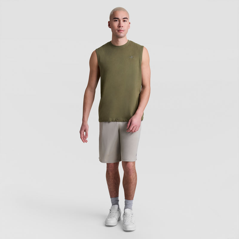 A person with a shaved head wears a Champion Muscle Tank, C Logo, olive-green, paired with light gray athletic shorts, gray socks, and white sneakers, standing against a plain white background.