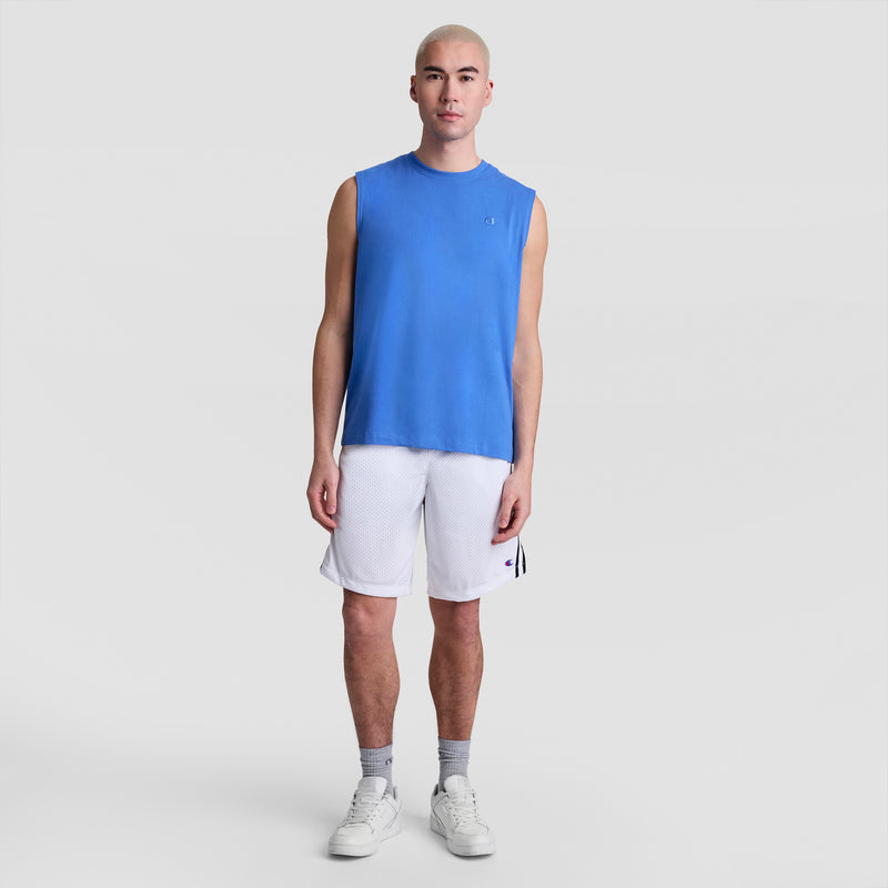 A person with a shaved head wears a blue Champion "Muscle Tank, C Logo," white athletic shorts, gray socks, and white sneakers, standing against a plain light gray background.