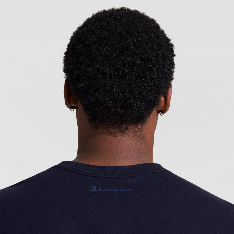 A person with short curly hair, seen from behind, wears a dark navy Champion Muscle Tank (C Logo - Big & Tall) with the brand name printed on the upper back. The background is light gray.