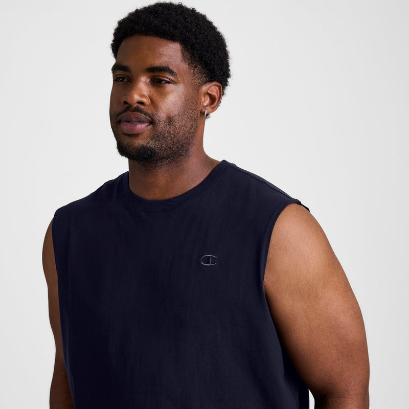 A man with short curly hair and a beard wears the Champion Muscle Tank, C Logo - Big & Tall, a sleeveless navy muscle tee with a small chest logo, standing against a plain light background.