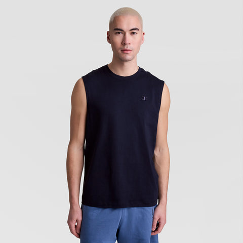 A person with short, light blond hair models the Champion Muscle Tank, C Logo—a sleeveless black top—paired with blue shorts against a plain light gray background, looking straight at the camera with a neutral expression.