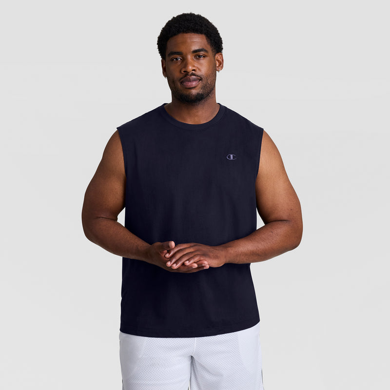 A man wears a sleeveless black Champion Muscle Tank, C Logo - Big & Tall, with white shorts, standing against a plain light gray background facing forward with his hands clasped.
