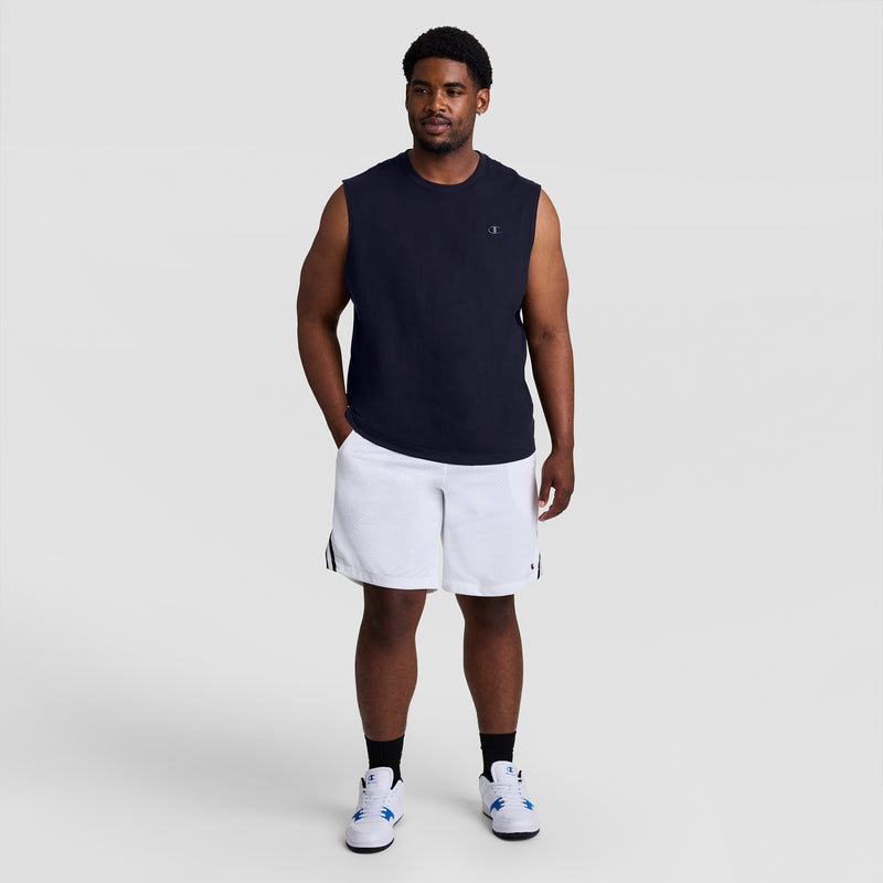 A man stands facing forward in a black Champion Muscle Tank, C Logo - Big & Tall, white athletic shorts, black socks, and white sneakers with blue accents against a plain light gray background.
