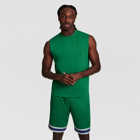 A man stands against a plain background, facing forward with hands together, wearing a green Champion Muscle Tank with C Logo and matching athletic shorts featuring white and dark blue stripes at the hem.