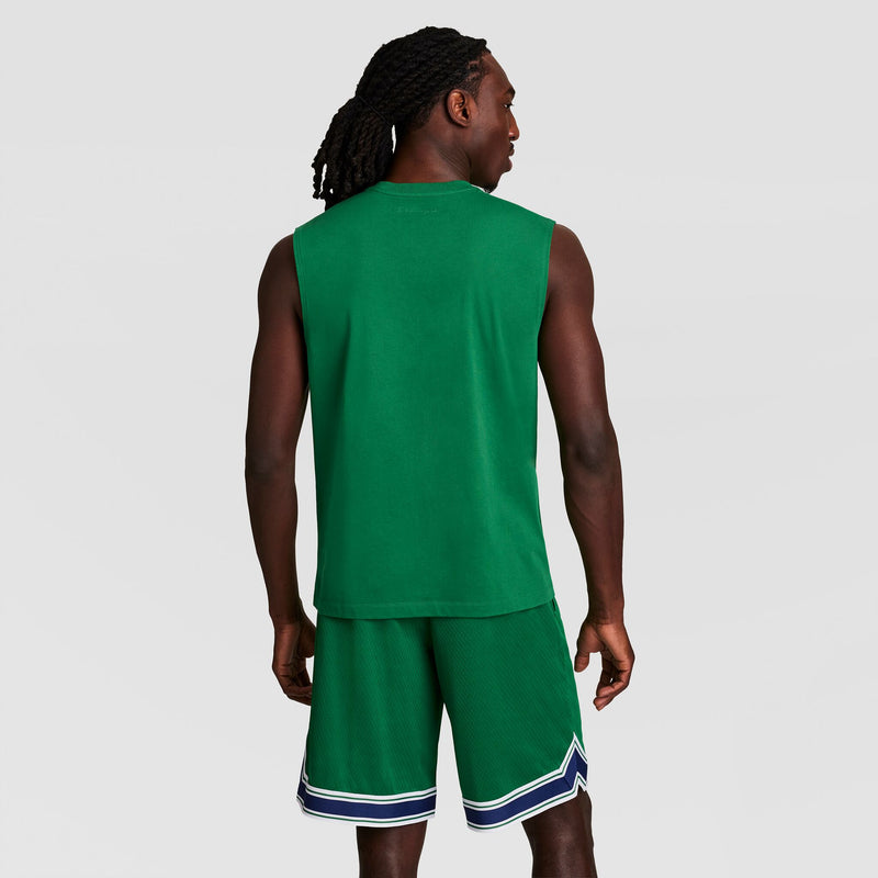 A person with long braided hair faces away from the camera, wearing a green Champion Muscle Tank, C Logo, and matching green athletic shorts with blue and white trim. The background is plain light gray.