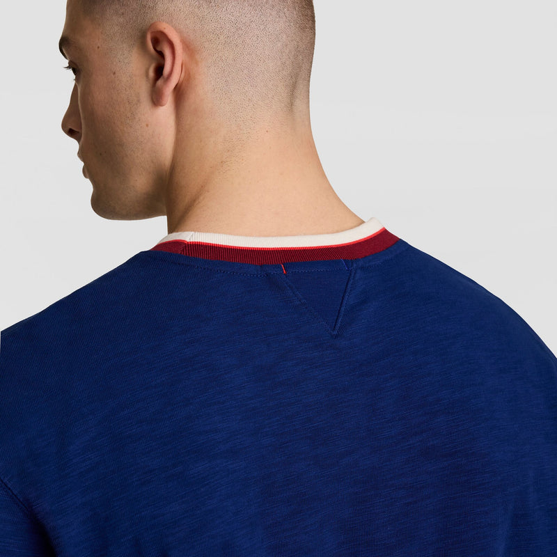 A person shown from behind wears a blue Champion Modern Retro Washed Crew Sweatshirt, C Logo, with a white and red ribbed collar. The textured slub cotton adds vintage streetwear flair against a plain light background.
