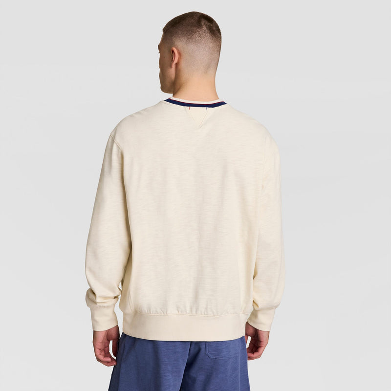 A person with short hair stands with their back to the camera, wearing a Champion Modern Retro Washed Crew Sweatshirt, C Logo, and blue shorts against a plain light gray background.