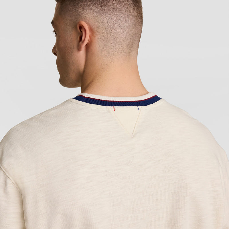 A man with short hair is seen from behind wearing the Champion Modern Retro Washed Crew Sweatshirt, featuring a cream color, blue/red/white striped neckline, V-shaped stitching below the collar, and the signature C Logo.