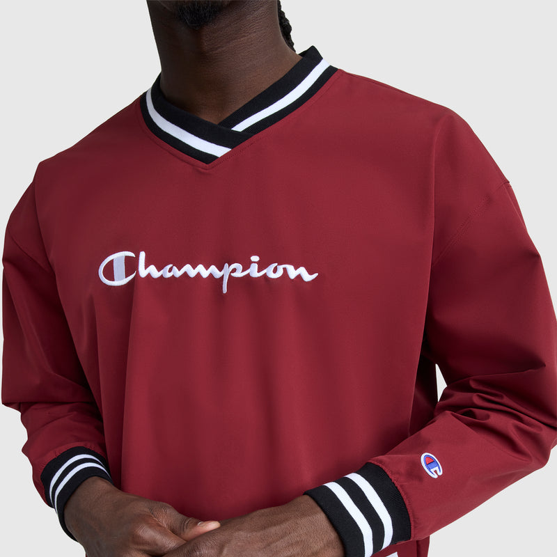 A person wears a maroon Champion Gridiron V-Neck Pullover with black and white striped cuffs and collar. The chest features an embroidered Champion logo, and a small C logo accents the left sleeve. The face is not visible.