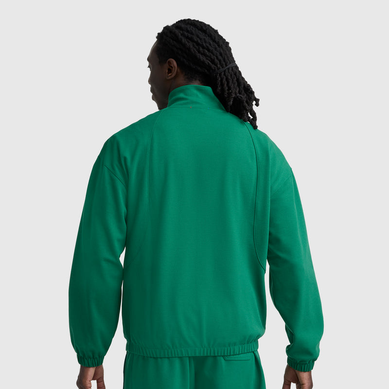 A person with long, dark, braided hair is seen from the back wearing a green Champion Gameday Full Zip Mock Neck, C Logo jacket and matching pants against a plain light gray background.