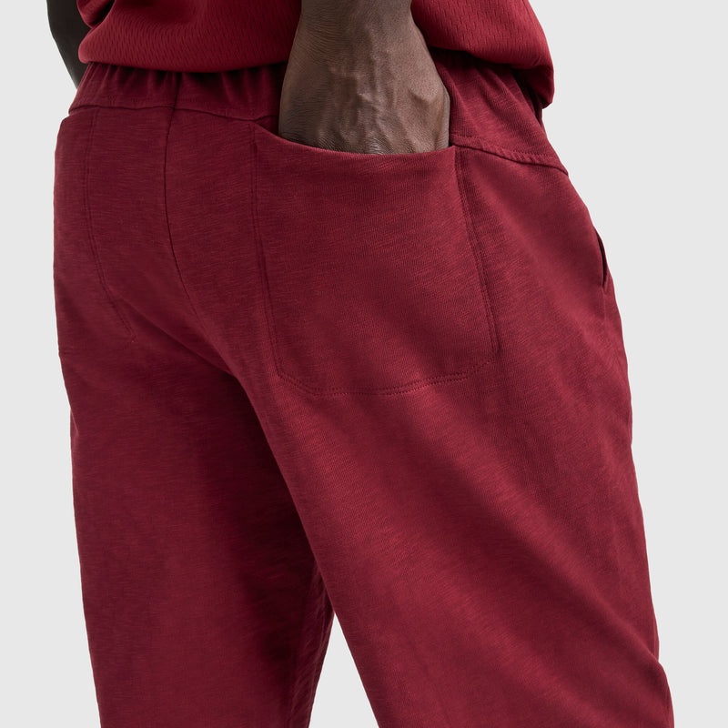 A person wears Champion's Modern Retro Washed Pant with C Logo in red, right hand in pocket, shown waist-down against a light gray background.