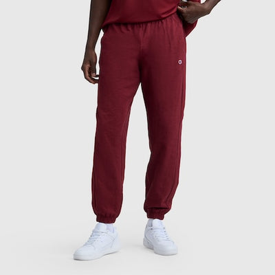 A person wearing maroon jogger sweatpants, a matching maroon shirt, and white sneakers stands against a plain light gray background. Only the lower half of their body is visible.