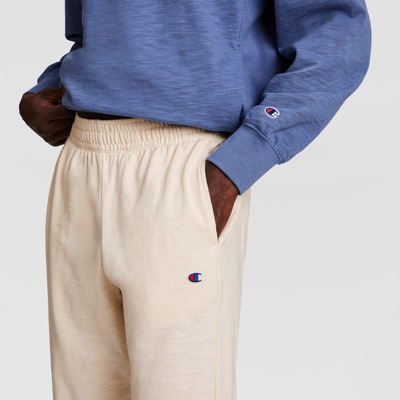 A person wears a blue sweatshirt and Champion Modern Retro Washed Pant, C Logo, with hands in pockets. Both garments show Champion embroidery. The image is cropped from shoulder to mid-thigh.