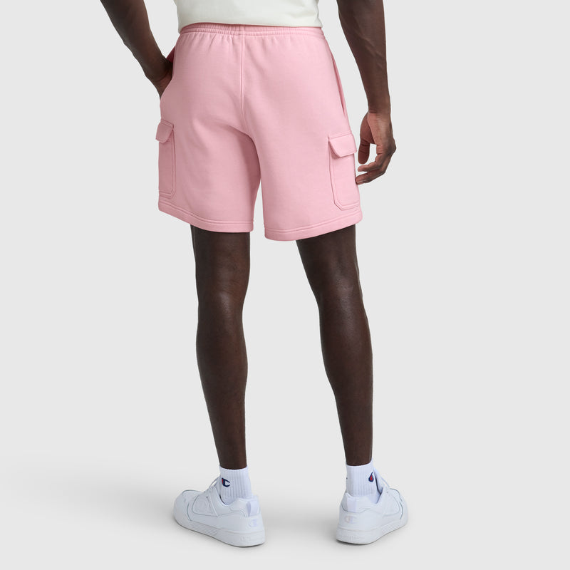 A person is shown from the back against a plain white background, wearing Champion's 8" Fleece Cargo Short with C Logo in light pink, paired with white crew socks and white sneakers.
