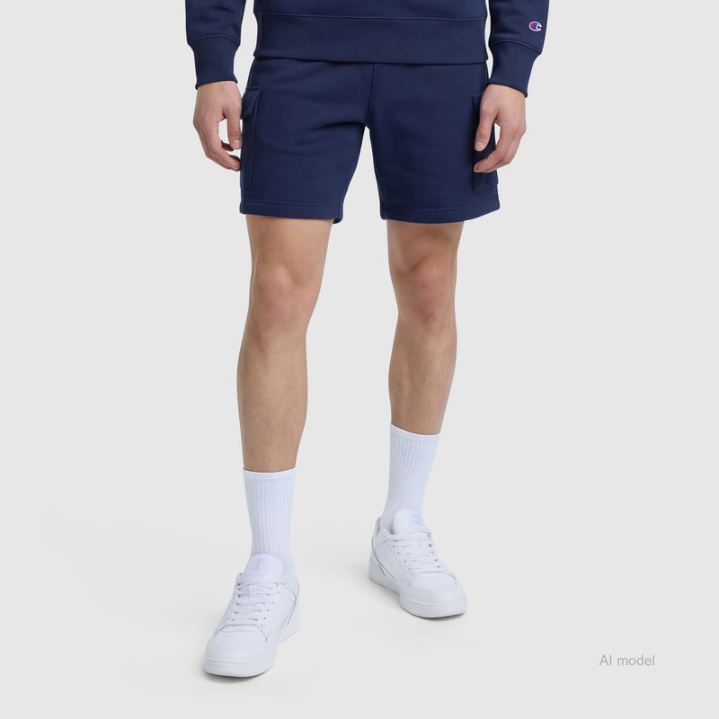 A person stands against a plain light background wearing Champion's 8" Fleece Cargo Shorts with the C Logo in navy blue, paired with a matching sweatshirt, white crew socks, and white sneakers.
