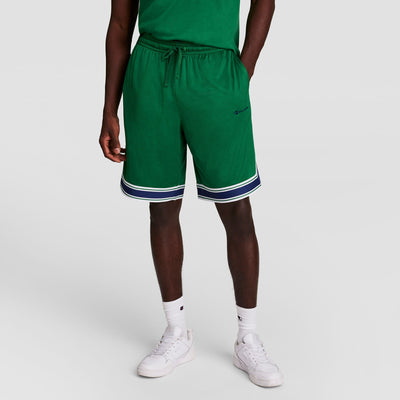 A person wearing a green t-shirt, matching green shorts with white and navy trim, white crew socks, and white sneakers, standing against a plain light background.