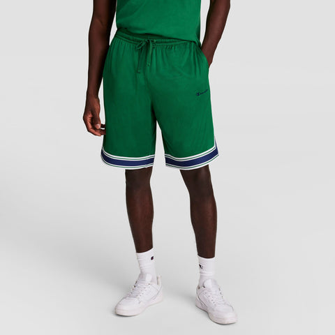 A person wearing a green t-shirt, matching green shorts with white and navy trim, white crew socks, and white sneakers, standing against a plain light background.