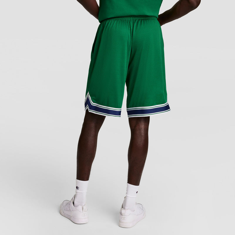 A person wearing green athletic shorts with white and navy stripes at the hem, white crew socks, and white sneakers, standing with hands on hips, shown from the back against a plain background.